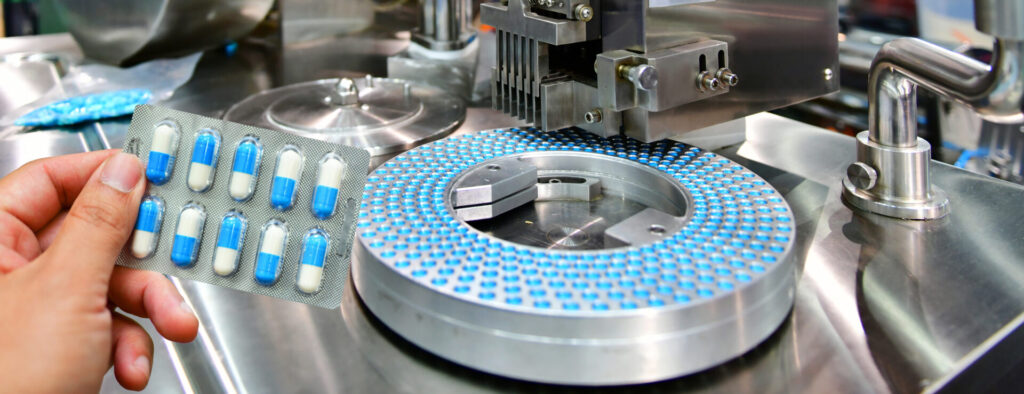 Hand holding blue capsule pack at medicine pill production line, Industrial pharmaceutical concept.